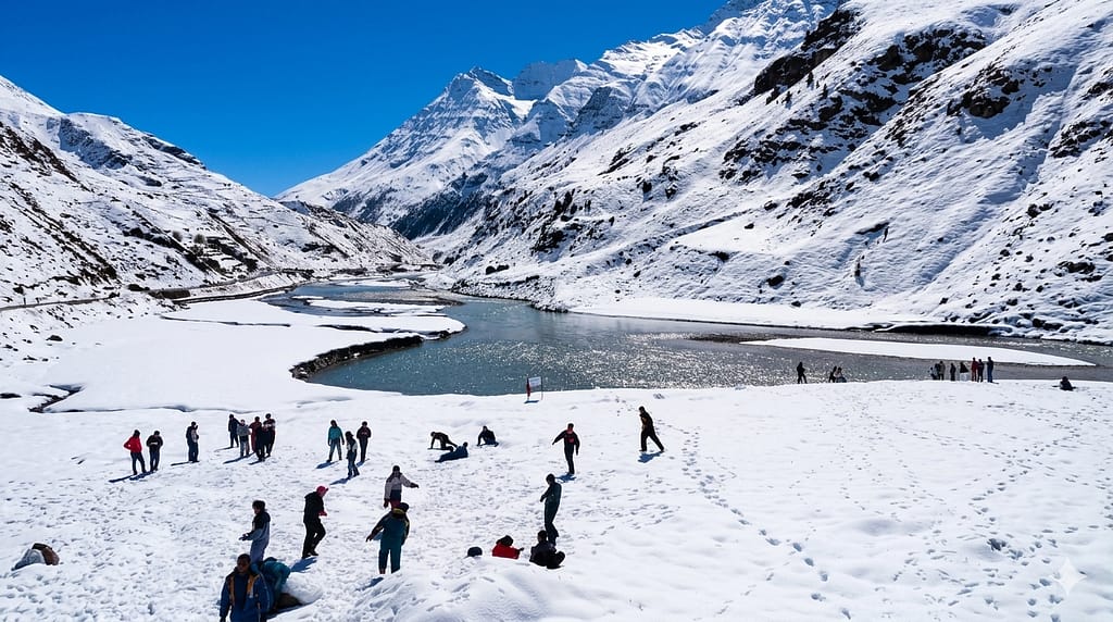 ourists enjoying a snowy landscape in Sissu Valley next to a flowing river with high mountains in the background.