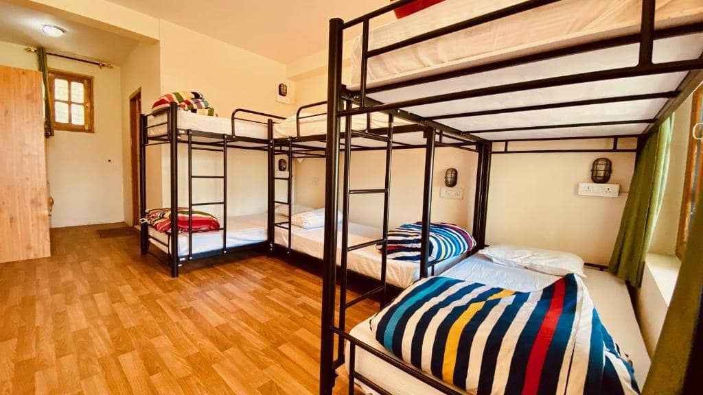 A clean and organized hostel dormitory with black metal bunk beds and colorful striped blankets.