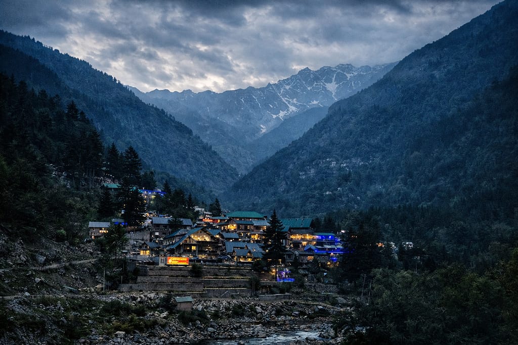 A peaceful evening view of houses nestled in a valley with mountains rising in the distance under a cloudy sky.