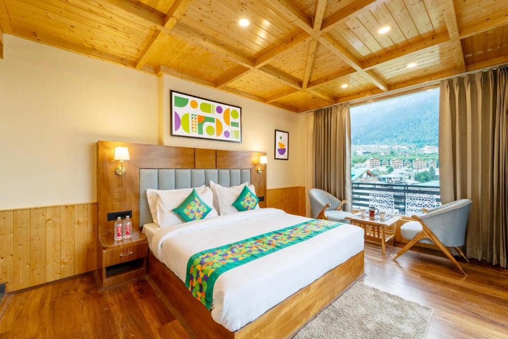 A modern hotel room with clean wooden decor, colorful pillows, and a large window view of the town.